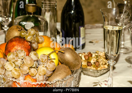 Früchte in einem Kristall Vase, ein Glas Champagner, ein Schälchen mit Nüssen, Rosinen und Erdnüsse auf einem festlich gedeckten Tisch Stockfoto