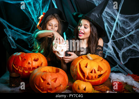 Halloween Konzept - schönen weißen Mutter mit glücklichen kleinen Tochter genießen mit Halloween Süßigkeiten und süße über Fledermäuse und Spinnennetz auf schwarz Studi Stockfoto