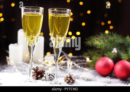 Zwei Gläser Sekt oder Saft auf dem Tisch, mit einem glühenden Girlande, rote Kugeln dekoriert, a Christmas tree branch und weißen Kerzen. Stockfoto