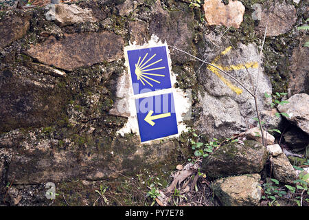 Camino de Santiago Fliesen auf Steinmauer. Jakobsweg Zeichen. Pfeil und Shell Stockfoto