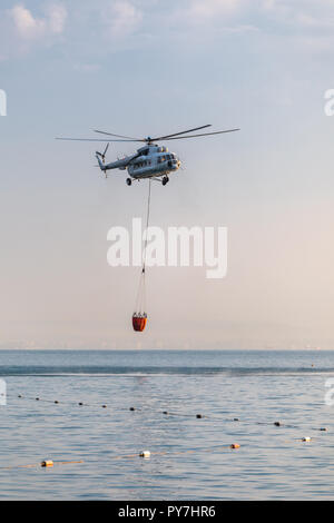 Ein Hubschrauber mit einem roten Korb ist über das Meer gesenkt Wasser aufzufangen. Stockfoto