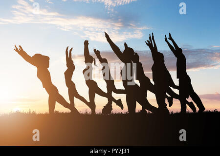 Silhouette von Menschen Yoga Gegen dramatische Himmel bei Dämmerung Stockfoto