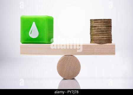 Grün Cubic Block mit Wassertropfen Symbol und gestapelte Münzen Balancing auf Holz- Wippe Stockfoto