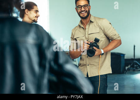 Fotograf in einem Studio mit einer Kamera in der Hand und lächelt. Fotograf shooting am Laptop. Stockfoto