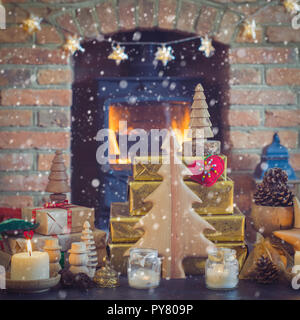 Weihnachten Zusammensetzung, Tannenzapfen in Weidenkorb, Holz- Ornamente, Kerzenlicht mit Fell Äste auf dem Tisch vor einem Kamin Kaminofen Stockfoto