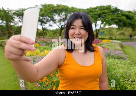 Schöne Übergewicht asiatische Frau unter selfie mit Handy im Park Stockfoto