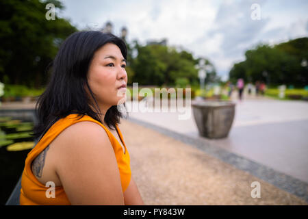 Profil anzeigen von Übergewicht asiatische Frau sitzen und denken in Park Stockfoto