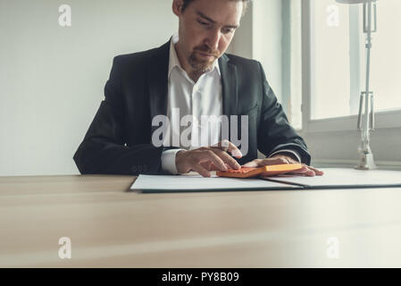 Retro Bild einer jungen Geschäftsmann mit einem Bart mit Taschenrechner, wie er in seinem Büro Schreibtisch Dokumente sitzt. Stockfoto