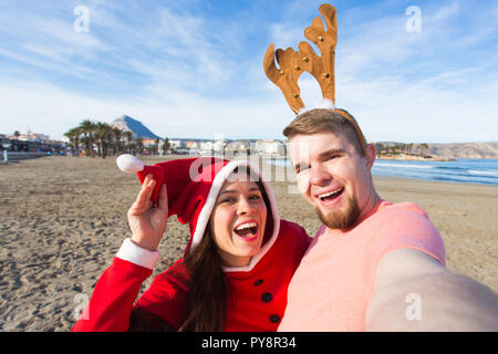 Spaß und Winterurlaub Konzept - glückliches Paar in Weihnachten Kostüme unter selfie über Sandstrand Hintergrund Stockfoto