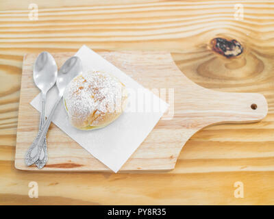Köstliche eclairs mit Puderzucker bestreut und Löffel auf Holz Schneidebrett auf Tabelle Ansicht von oben. Stockfoto
