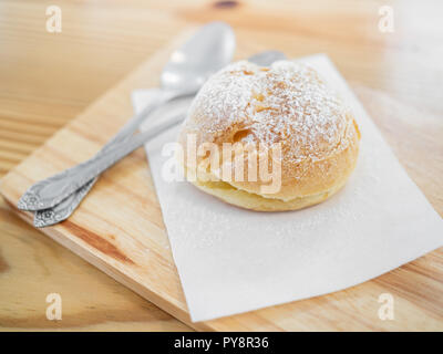 Köstliche eclairs mit Puderzucker bestreut und Löffel auf Holz Schneidebrett auf Tisch. Stockfoto