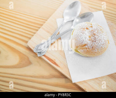 Köstliche eclairs mit Puderzucker bestreut und Löffel auf Holz Schneidebrett auf Tisch. Stockfoto