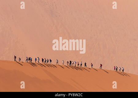 Namibia Tourism - Touristen wandern auf dem Kamm einer Düne; Big Daddy Dune im Hintergrund; Sossusvlei, Namib, Namibia Afrika Stockfoto