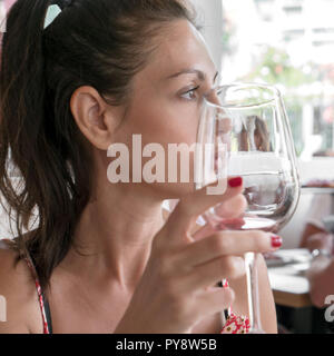 Junge Frau mit einem natürlichen Make-up und einen Pferdeschwanz hält ein rotes Glas Wein. Defokussierten verschwommenen Hintergrund. Stockfoto