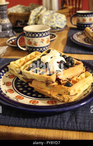 Einen Teller mit Waffeln, Blaubeeren und Sahne auf einem Frühstückstisch Stockfoto