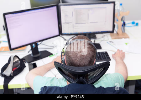 Ein Mann bei der Arbeit am Computer in eine IT-Büro, zwei Monitore vor sich auf den Schreibtisch. Stockfoto