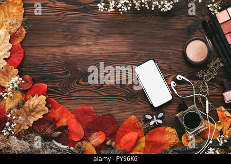 Weibliche Zubehör eingestellt. Blätter im Herbst, Smartphone und Kopfhörer auf hölzernen Hintergrund Stockfoto