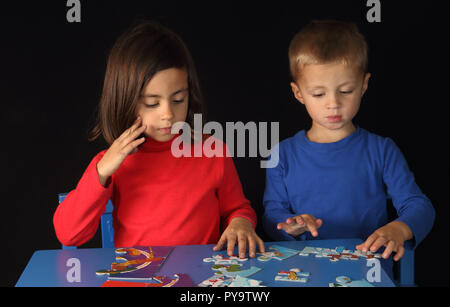 Bruder und Schwester spielen Mit einem Puzzle auf einer blauen Tabelle mit einem schwarzen Hintergrund Stockfoto