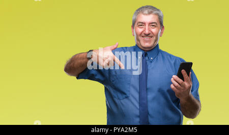 Gut aussehender älterer Mann sms senden Nachricht mit Smartphone über isolierte Hintergrund mit Überraschung Gesicht zeigenden Finger zu sich selbst Stockfoto