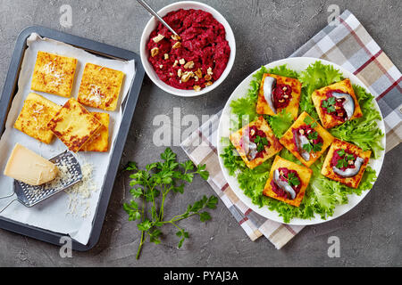 Plätze mit cremiger Polenta rote Bete pürieren, mit Sardellen und Petersilie auf einer weißen Platte gekrönt. frisch gebackene polenta Bars und Parmesan auf ein Backblech tr Stockfoto