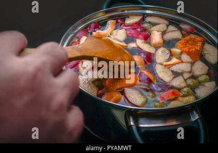 Mitreißend bunte Apfelscheiben, Orangen, Frucht Mix in einem Topf mit Löffel aus Holz. Gesunde Essgewohnheiten. Erfrischende Frucht Apfelwein Punsch Party Trinken. Stockfoto