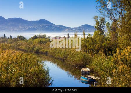 Kleiner Fluss mit Fischerbooten und Vegetation, Berge im Hintergrund Stockfoto