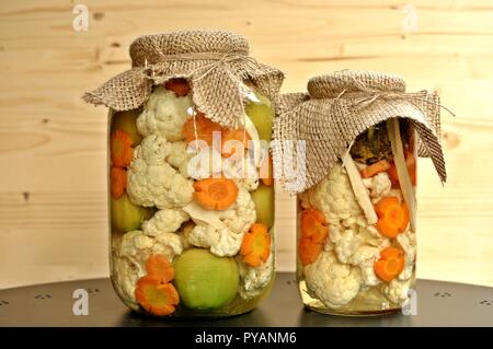 Konzept der zwei saisonalen Pickles jar mit grün gefärbt rohe Tomaten, orange Karotte und weißen Blumenkohl auf natürlichen Holz- Hintergrund. Stockfoto