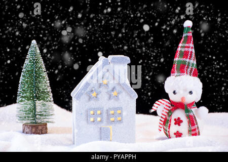 Weihnachten nacht Idylle mit kleinen Haus Spielzeug und Schneemann und Tannenbaum. Es schneit und Schneeflocken fallen. Winter und Urlaub Konzept Bild Stockfoto
