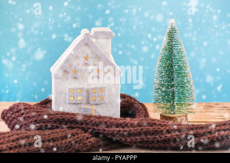 Weihnachten Spielzeug house Wrapped in warmer Schal und grünen Xmas Tree, es schneit auf blauem Hintergrund. Winter Saison und Idylle Konzept Stockfoto