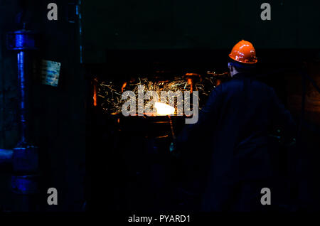 Industrielle Arbeiter in der Fabrik schweißen Nahaufnahme. Heiße Eisen in den weiterverarbeitenden Betrieben, die ein Arbeitnehmer statt. Eisen schmelzen Recycling arbeiten. Rolle von heißem Metall. Schwere schmieden Stockfoto