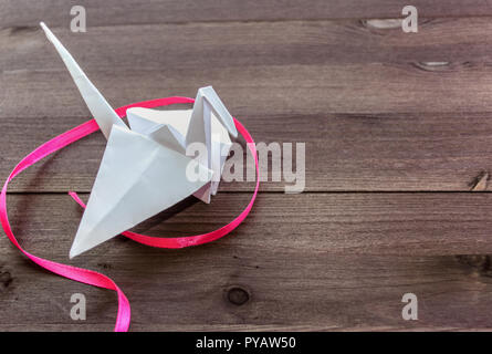 White paper Crane von Pink Ribbon Kurven auf dunklem Hintergrund umgeben Stockfoto