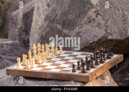Schachbrett mit Schachfiguren auf Stein mit großen Felsen im Hintergrund. Im freien Spiel Schach Stockfoto