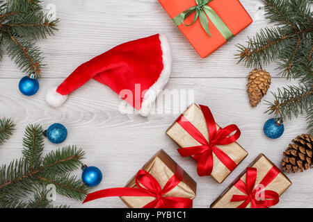 Weihnachtsdekoration. Geschenkboxen, Santa's Hut, tanne baum Zweige mit Zapfen auf grauem Hintergrund. Ansicht von oben. Weihnachten Grußkarten-Konzept. Stockfoto