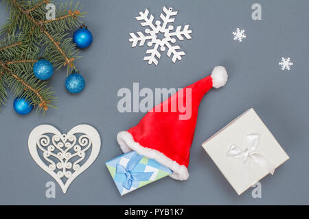 Weihnachtsdekoration. Geschenkboxen, Santa's Hut, tanne baum Zweige mit Zapfen auf grauem Hintergrund. Ansicht von oben. Weihnachten Grußkarten-Konzept. Stockfoto