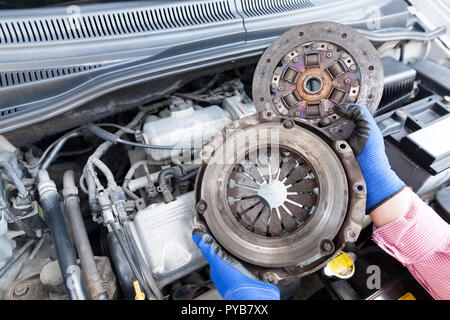 Automechaniker Tragen von Handschuhen mit einem alten Kupplungskorb und Motor der Platte über den Auto Motor Stockfoto