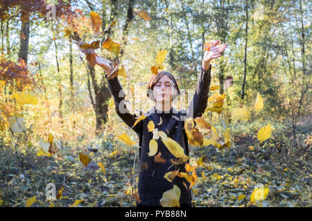 Frau wirft gelben Blätter im Herbst in der Luft. Porträt einer jungen Frau mit geschlossenen Augen und bunte Blätter fliegen um Ihr Stockfoto