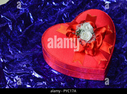 Geschenkverpackung in leuchtend rote Seide Farbe in Form von ein Herz und eine Blume zu beugen. Valentinstag. Glühende abstrakte Schwarz und Violett abstrakte Textur. C Stockfoto