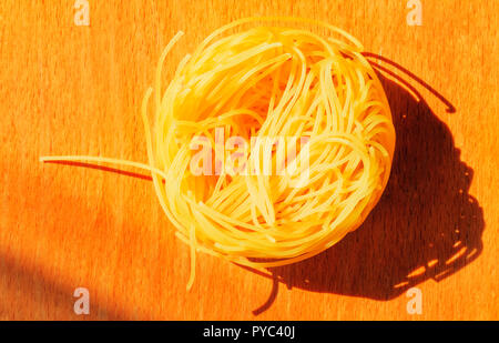 Ein schönes Nest von Angel hair Pasta auf einer hölzernen Hintergrund, dünne Bänder von Teigwaren wie Nudeln, Pasta Schatten auf dem Brett, Ansicht von oben, helle Farbe Stockfoto