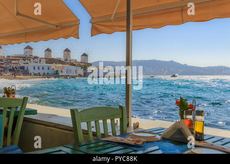 Mykonos, Panoramablick auf weißen berühmten Windmühlen Stühle mit Tischen im typisch griechischen Restaurant von Klein Venedig Insel der Kykladen, Griechenland. Stockfoto