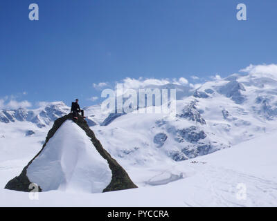 Backcountry skier sitzen auf einem großen schneebedeckten Felsen inmitten einer spektakulären Winter Berglandschaft Stockfoto
