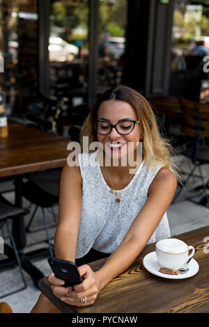 Lächelnd business Frau in ein Café im Freien holding Handy in den Händen. Stockfoto