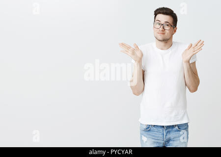 Sorry, mein Fehler. Portrait von dumm aussehenden jungen männlichen Modell zuckend mit erhobenen Händen in der Nähe von Schultern und leichten Grinsen, appologizing, Fehler oder nicht bewusst, was auf weißem Hintergrund geschieht Stockfoto