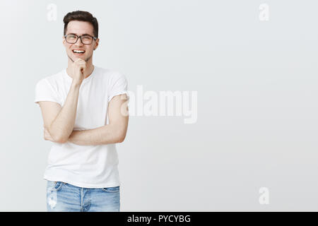 Erfolgreiche happy digital Nomad laut lachen, mit Freunden Zeit verbringen, anstatt im Büro, die Hand am Kinn lächelte breit Gefühl begeistert und optimistisch über grauer Hintergrund Stockfoto