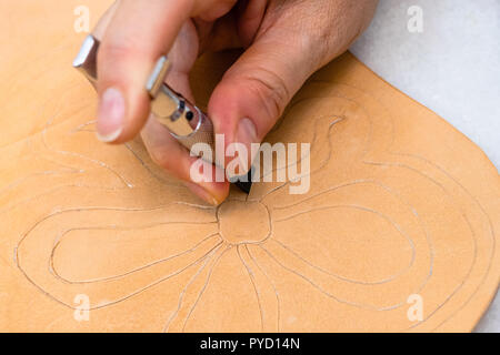 Workshop der geschnitzten Leder Tasche - Handwerker schnitzt Blume auf der Oberfläche des groben pflanzlich gegerbtes Leder durch Schwenken der Gegenschneide Stockfoto