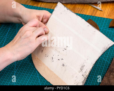 Workshop der geschnitzten Leder Tasche - Handwerker entfernt die schützendes Gewebe auf der Rückseite des Elements der Handtasche aus Leder Stockfoto