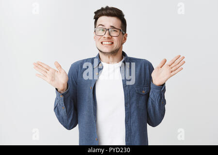 Es tut mir Leid, dass ich es vermasselt hätte. Schuldig Jungen und hübschen Mann in Gläsern und blaue T-Shirt heben die Hände in der Nähe von Schultern zuckend, awkard Lächeln, als Entschuldigung für die Fehler auf weißem Hintergrund Stockfoto