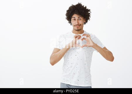 Liebe meine Freunde. Nett freundlich aussehende entspannt Hispanic Mann mit gebräunter Haut und Afro Frisur zeigen Herz Zeichen über Brust und lächelnd, während Zuneigung zeigen, Freundin, überraschung Datum Stockfoto