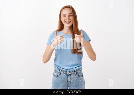 Stimme voll und ganz zu und unterstützen Sie. Portrait von freudiger Genugtuung gut aussehende rothaarige Frau mit Sommersprossen, Daumen und lächelnd unterstützend und Jubel geben positive Antwort über grauer Hintergrund Stockfoto