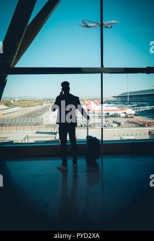 Ein junger und attraktiver Geschäftsmann sucht durch das Fenster in der Flughafen Terminal. Ein Flugzeug fliegt, während andere auf dem Grundstück geparkt werden Stockfoto