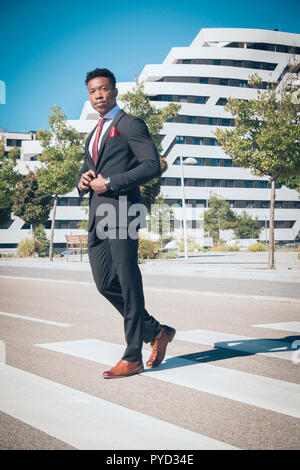 Nahaufnahme von einem jungen und attraktiven schwarzen Geschäftsmann zu Fuß in der Stadt, der vor der modernen Gebäuden formelle Kleidung tragen. Stockfoto